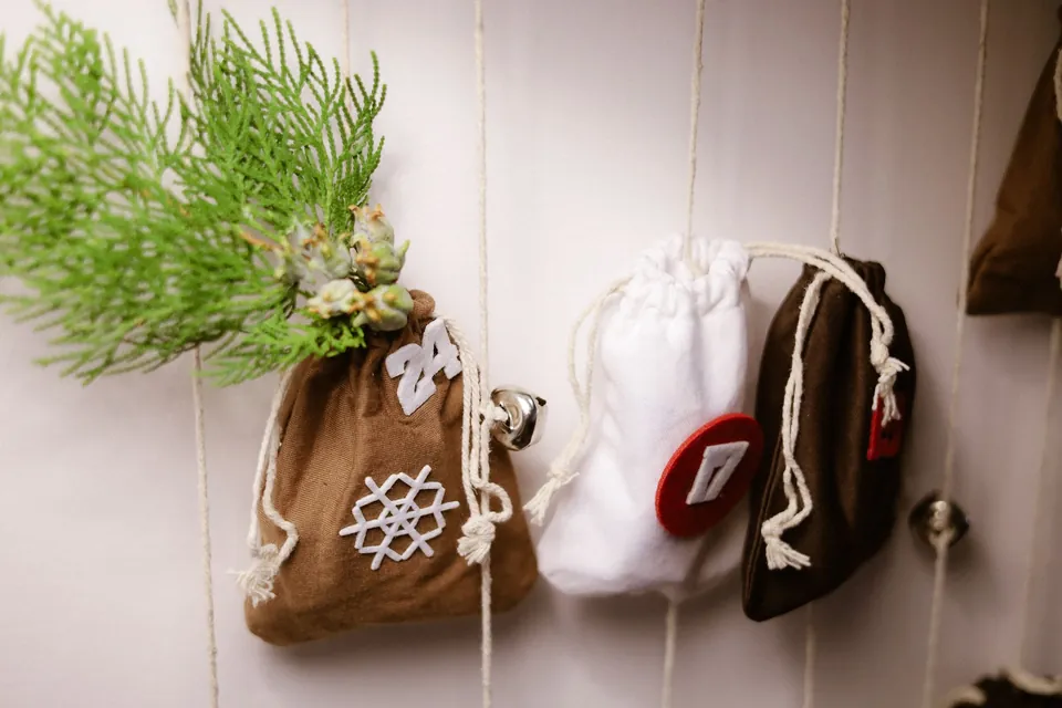 Handmade fabric advent bags with numbers and evergreen sprigs hanging on a wall