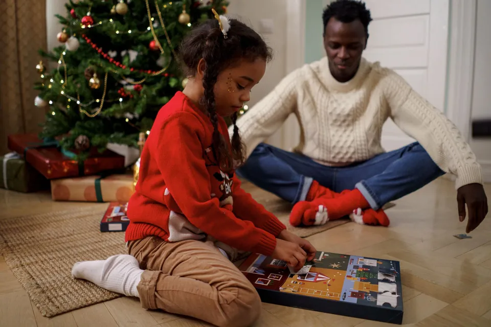A girl and her father opening an advent calendar beside the Christmas tree
