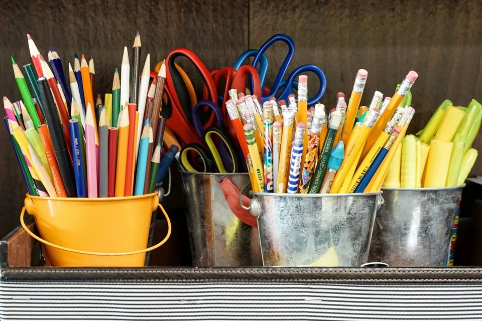 Colored pencils, scissors and markers sorted into metal buckets