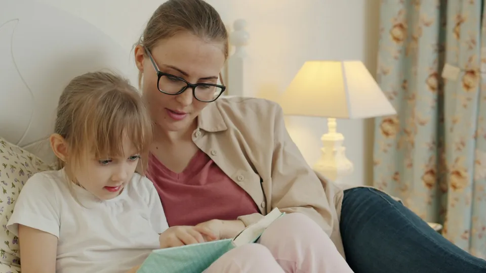 A mother and daughter reading a book together in bed