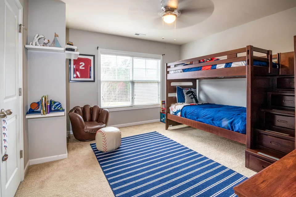 A child's bedroom with a wooden bunk bed, a striped rug and shelves of books