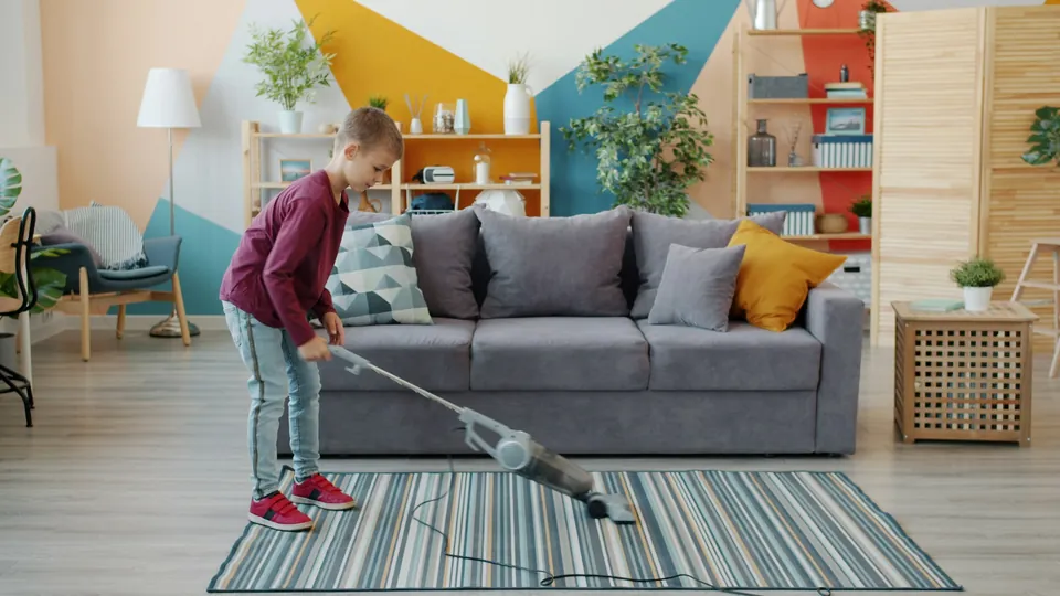 A young girl vacuuming a striped rug in the living room