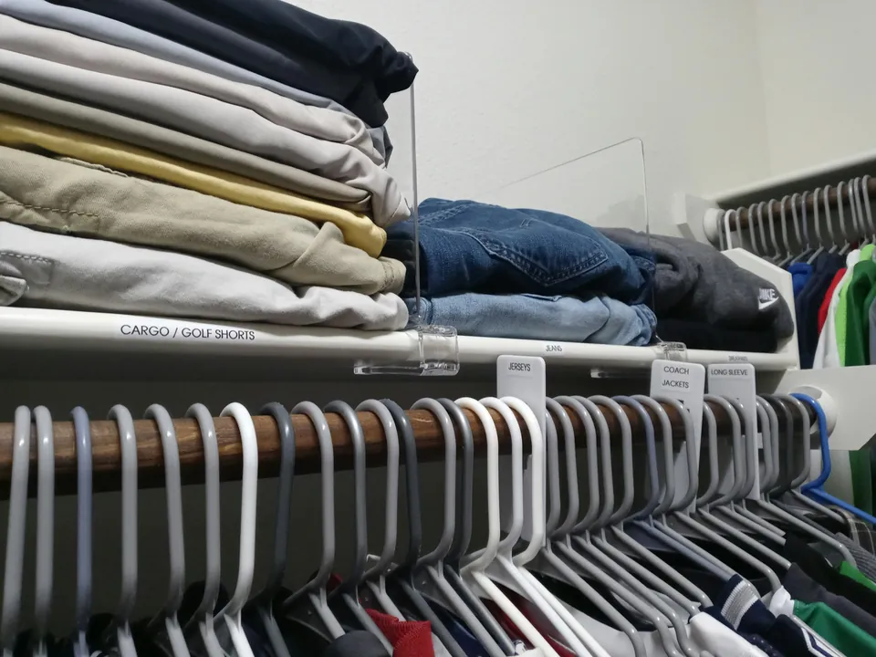 Stacks of folded clothing on a closet shelf above hanging clothes