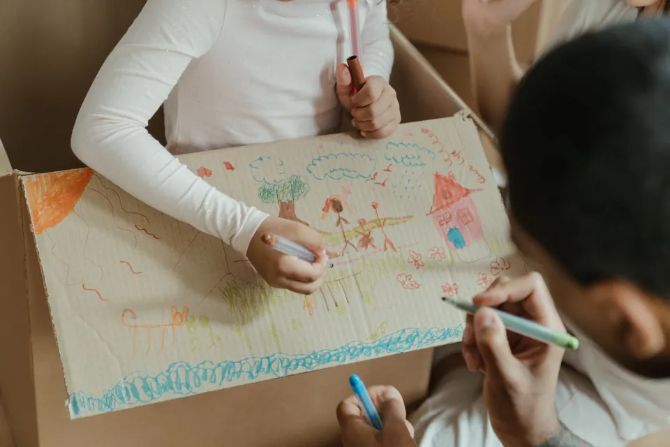 Children drawing with colored pens on the side of a cardboard box