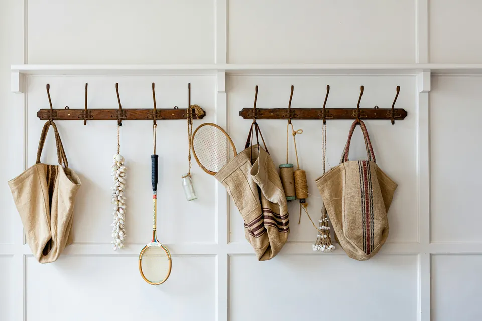 Tote bags and a tennis racket hanging from a row of wall hooks