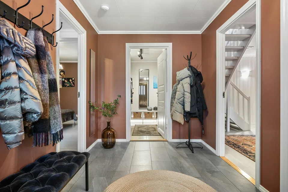 A hallway with coats on wall hooks and a padded bench