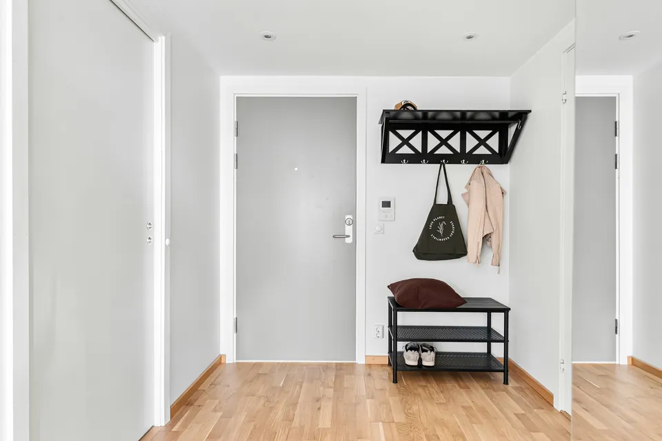 A small white hallway with a bench, shoe rack and wall hooks