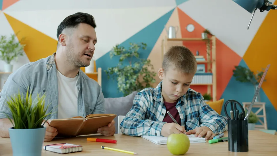 A father sitting beside his son as he does homework at a desk