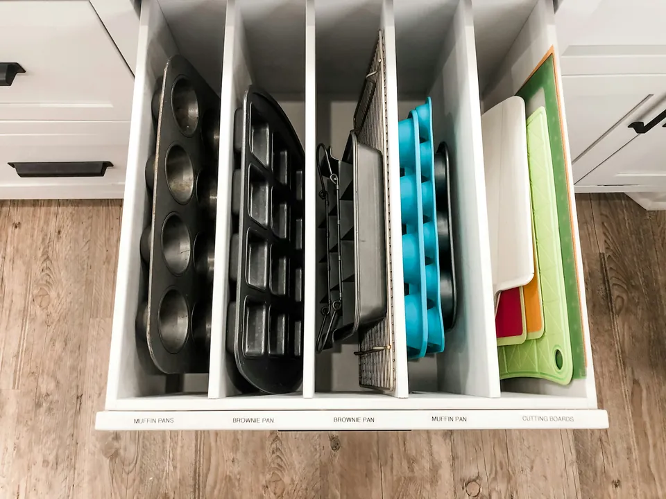 A kitchen drawer with vertical dividers holding baking pans and cutting boards