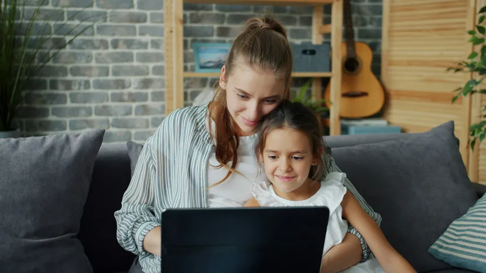 A mother and daughter sitting together on the sofa looking at a laptop