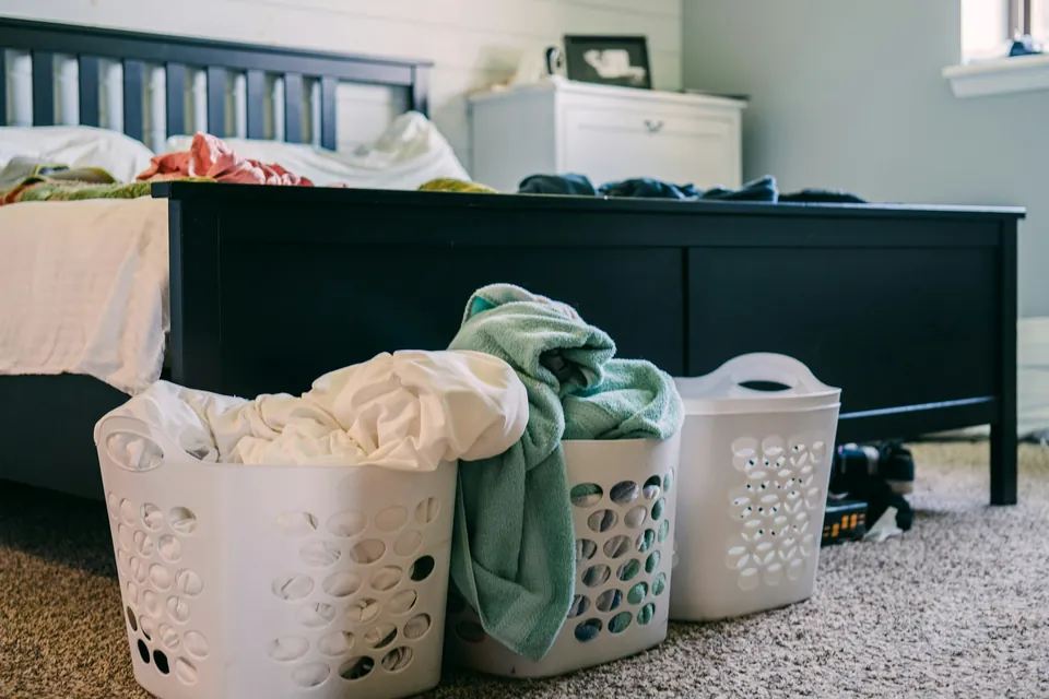 Three laundry baskets of clothes waiting beside a bed