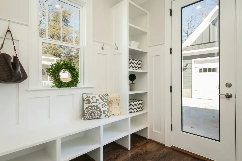 A white mudroom with cubbies, a built-in bench and hooks beside the back door