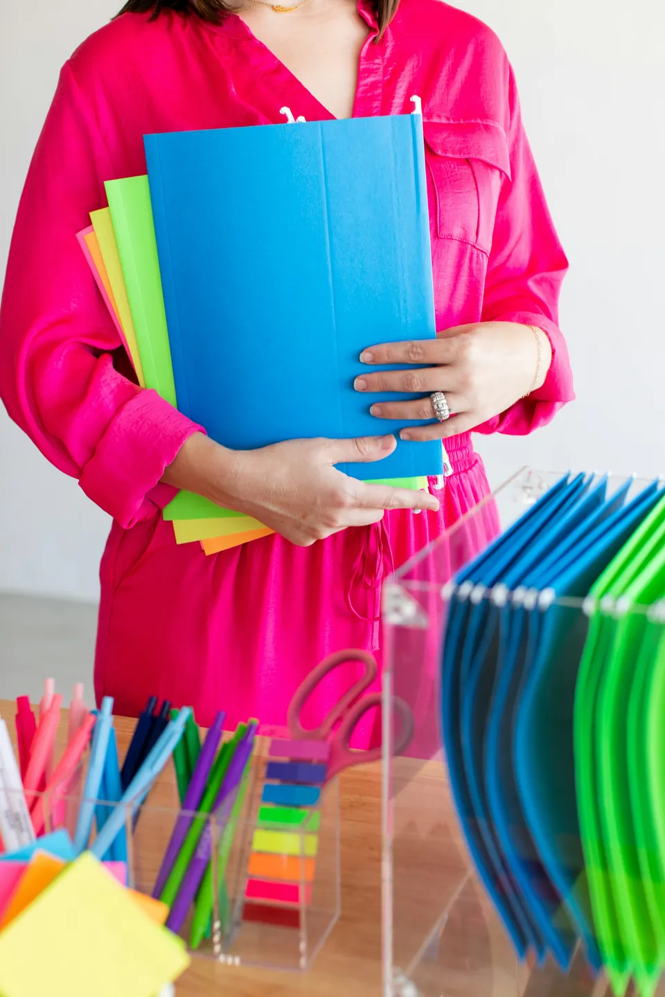 A person holding colorful file folders beside a desk
