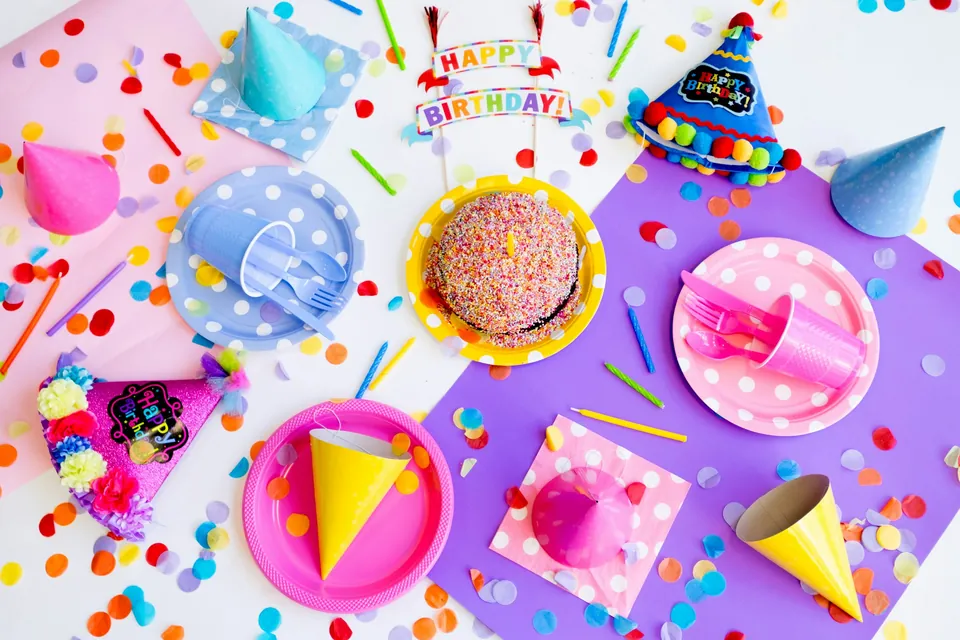 A birthday party table seen from above with paper plates, hats, cake and confetti