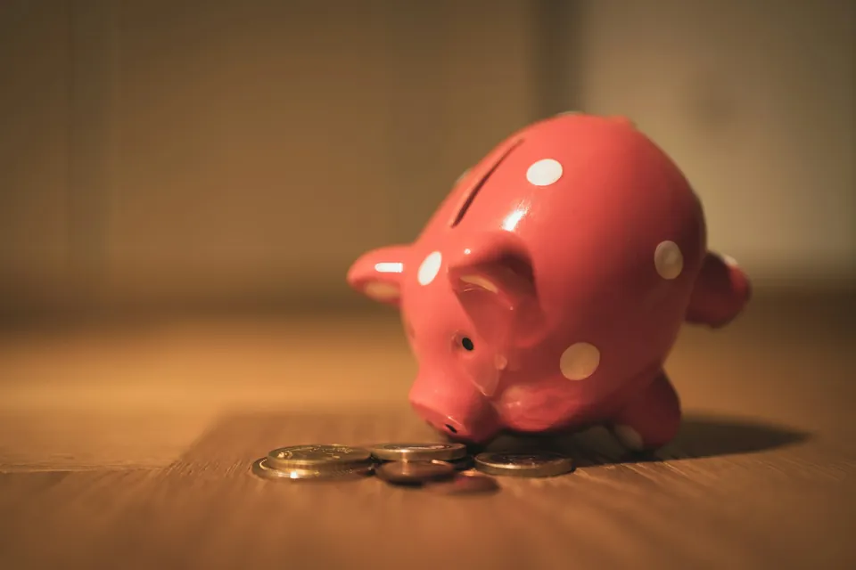 A pink piggy bank beside a few coins on a table