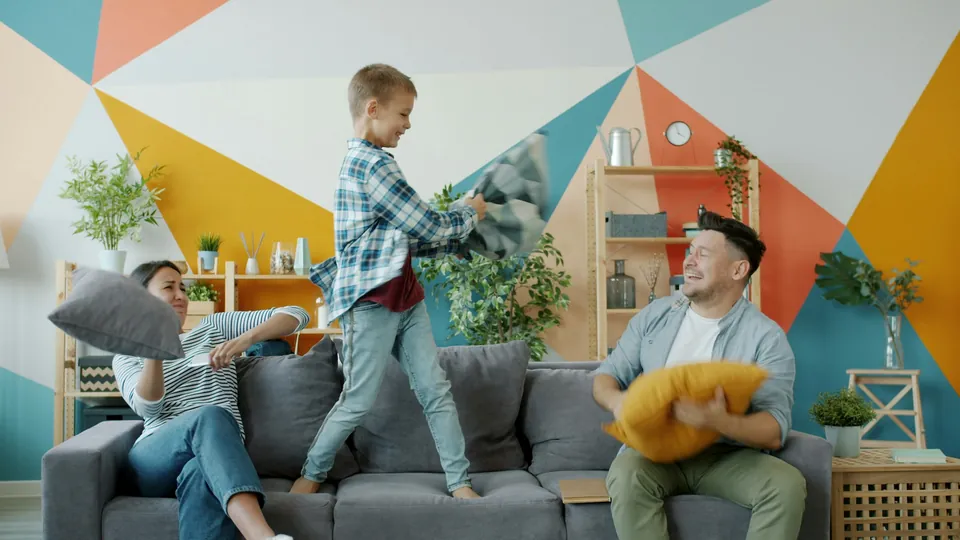 A family having a playful pillow fight on the living room sofa