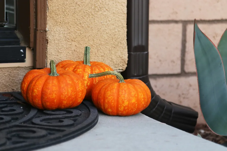 Three small pumpkins on a doorstep beside a dark front door