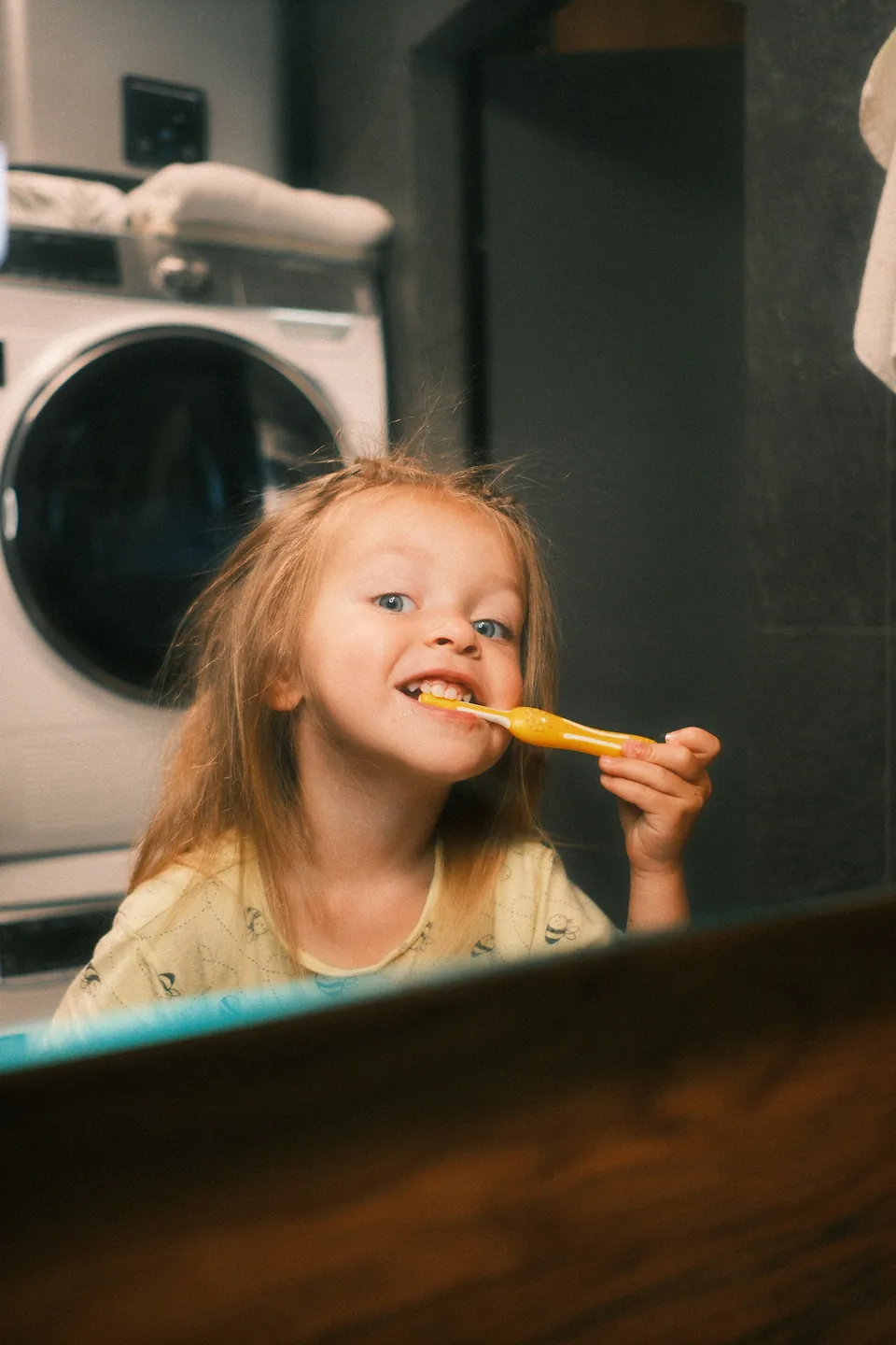 A young girl brushing her teeth in front of the bathroom mirror