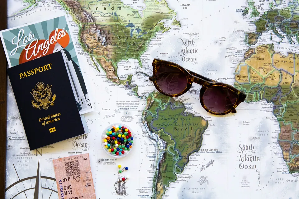 A passport, sunglasses and map pins laid out on a world map