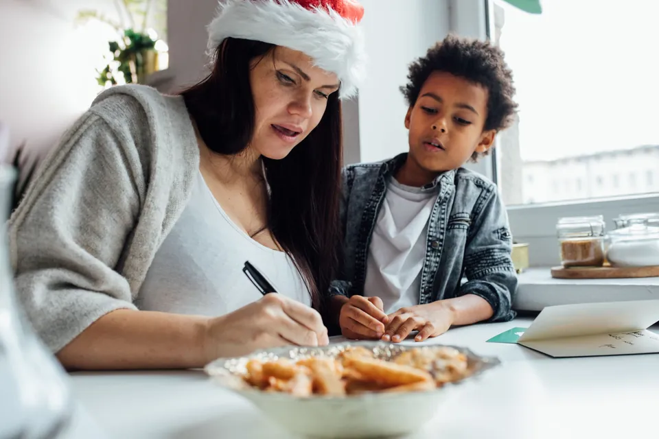 A mother and son writing holiday cards together at the kitchen table